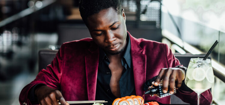 Masturdating: Is it self-care? - cheerful curly african guy holding chopsticks sushi rolls chinese food fish restaurant terrace - Shujaa Designs